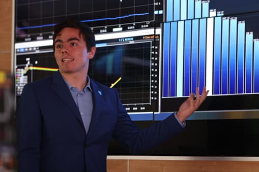 Ari Emilio Núñez presentando frente a pantallas con gráficas de datos [confirmar pie]